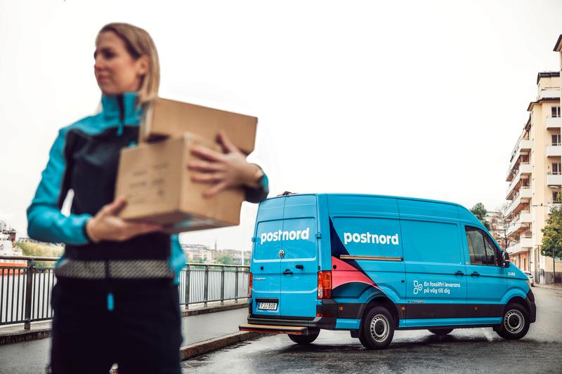 dame med pakke i armene bak blå Postnord leveringsbil