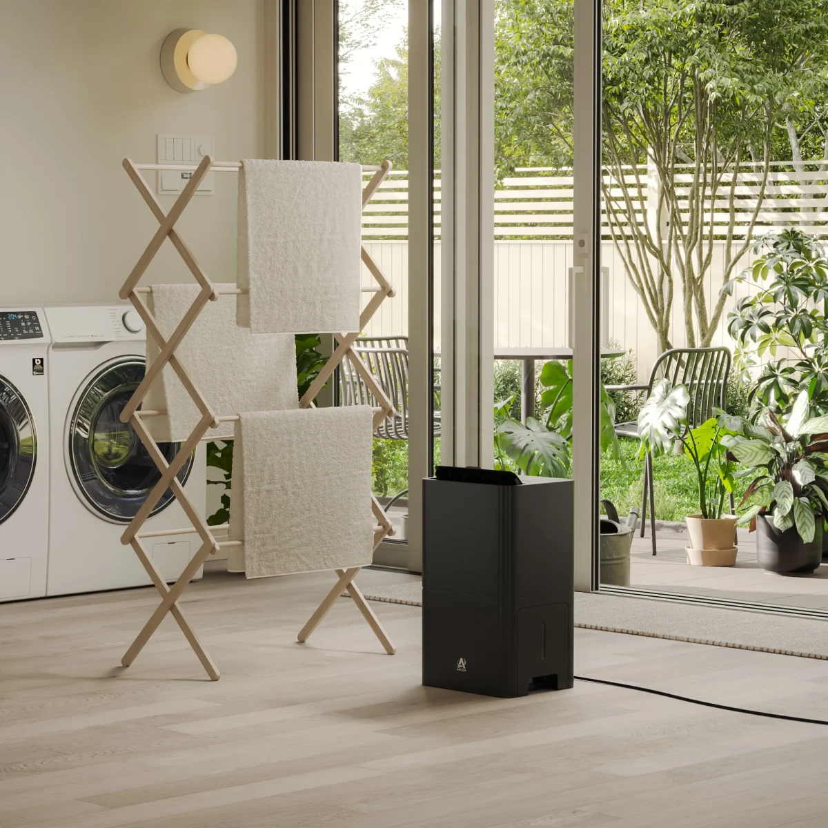 sort luftavfukter rettet mot håndkler på et tørkestativ foran vaskemaskin og tørketrommel på vaskerommet