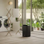 sort luftavfukter rettet mot håndkler på et tørkestativ foran vaskemaskin og tørketrommel på vaskerommet