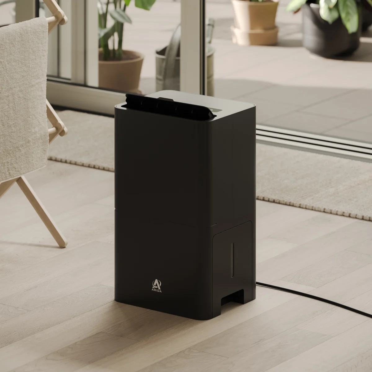 close up sort luftavfukter på gulv med spjelt opp rettet mot klesstativ med klær til tørk