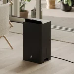 close up sort luftavfukter på gulv med spjelt opp rettet mot klesstativ med klær til tørk