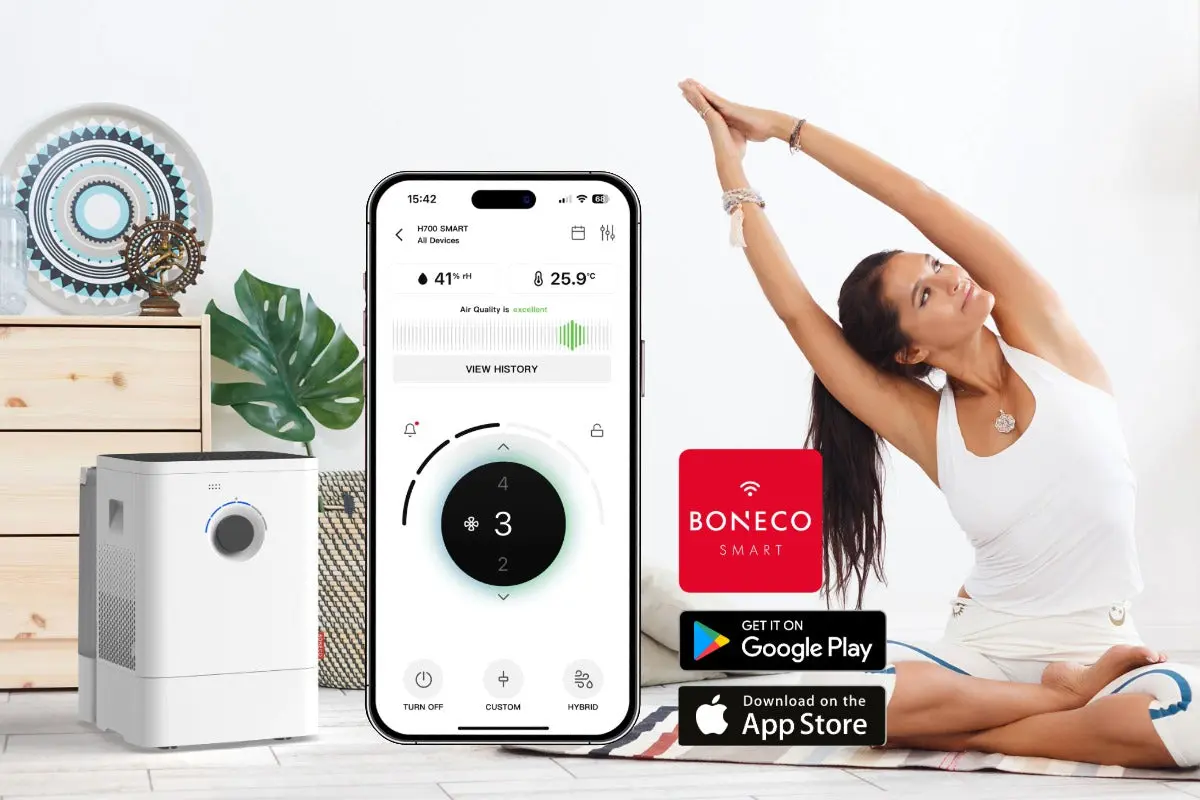 hvit luftvasker luftfukter med sort topp og betjeningp i stue ved siden av dame med mobiltelefon og app forklart